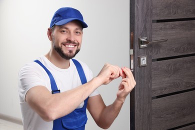 Worker in uniform with screwdriver repairing door lock indoors