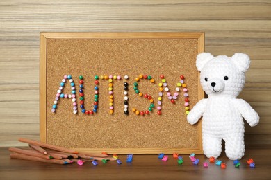 Photo of Cork board with word Autism made of colorful pins, pencils and toys on wooden table