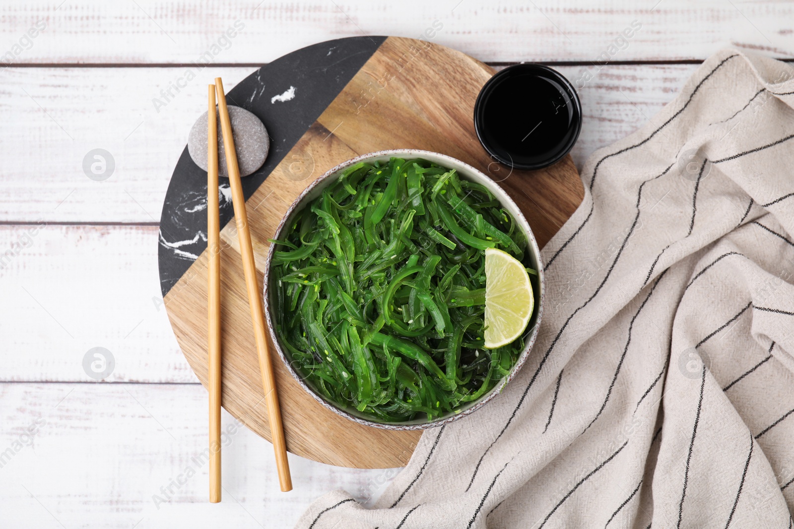 Photo of Tasty seaweed salad in bowl served on wooden table, flat lay