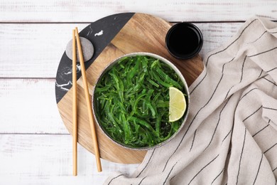 Photo of Tasty seaweed salad in bowl served on wooden table, flat lay