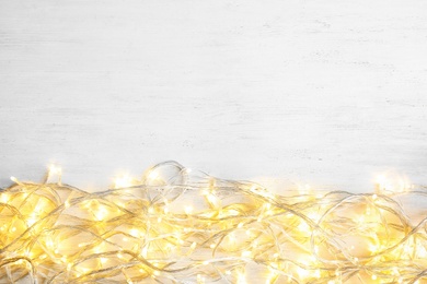 Photo of Glowing Christmas lights on wooden background, top view