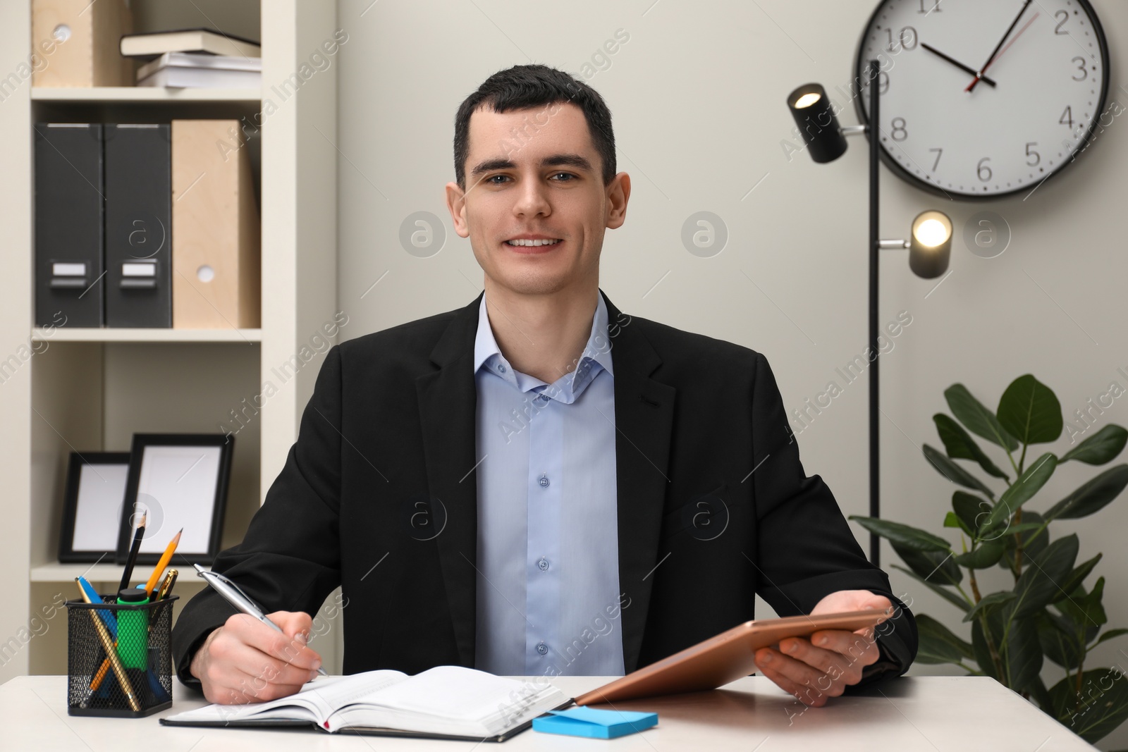 Photo of Man taking notes while using tablet at table in office