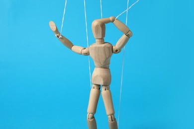 Photo of One wooden puppet with strings on light blue background