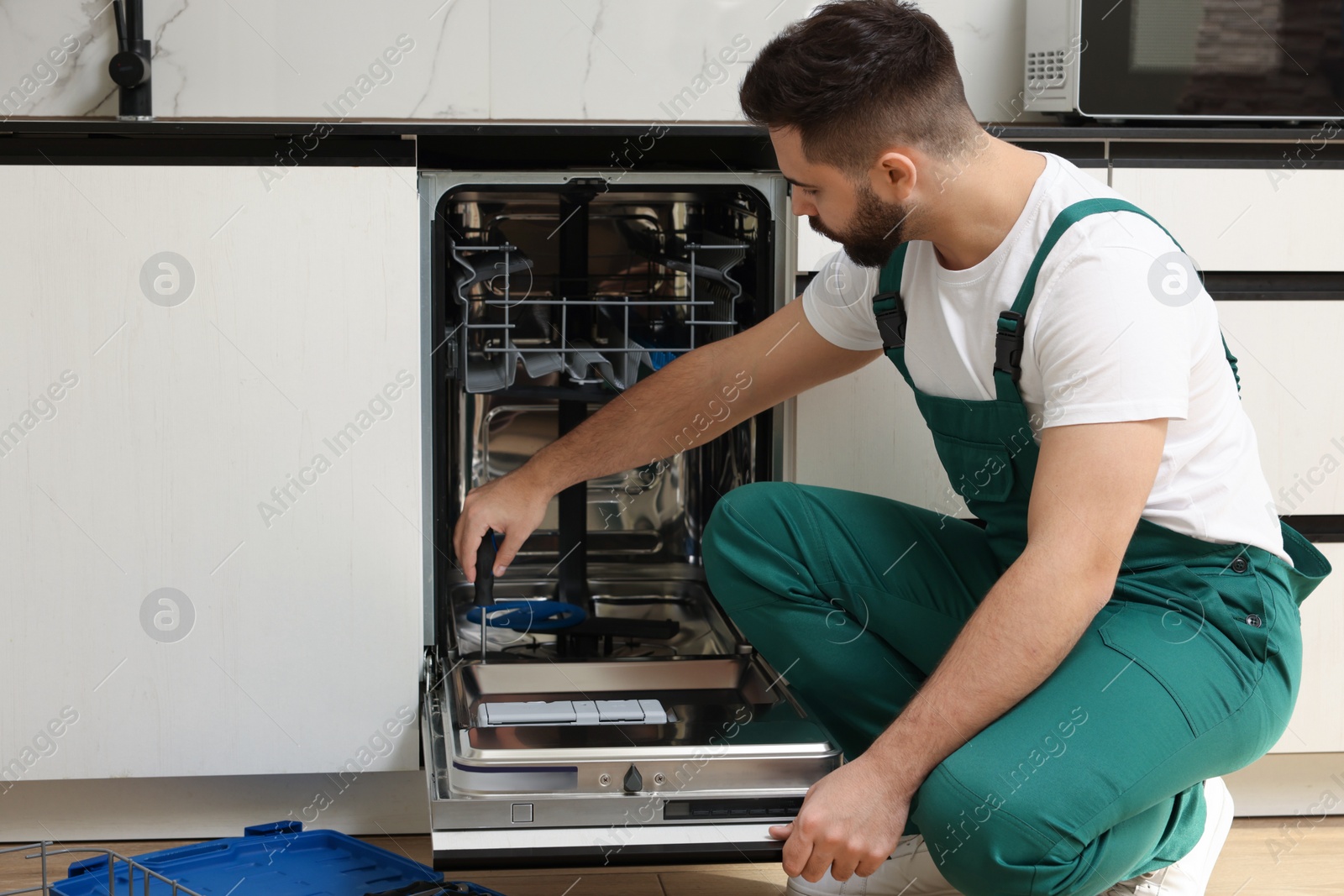 Photo of Serviceman repairing dishwasher door with screwdriver in kitchen