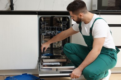 Photo of Serviceman repairing dishwasher door with screwdriver in kitchen