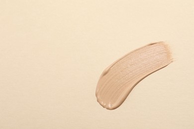 Smear of skin foundation on beige background, top view. Space for text