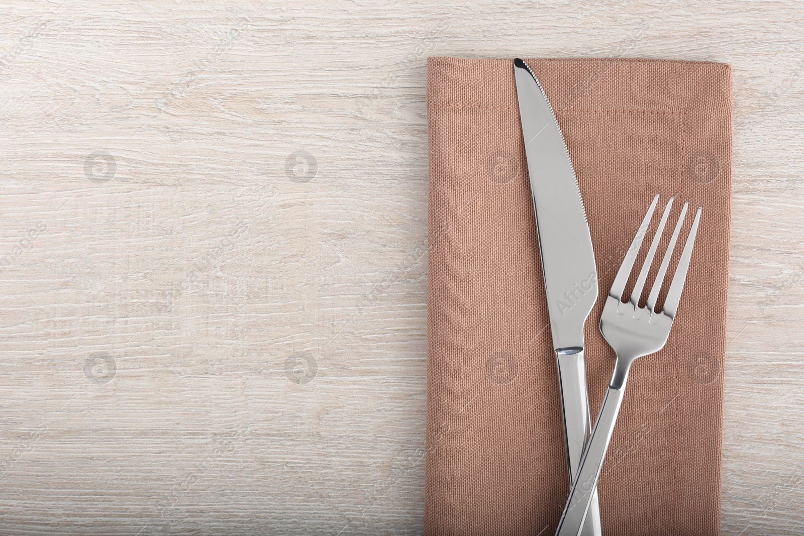 Photo of Shiny fork, knife and napkin on white wooden table, flat lay. Space for text