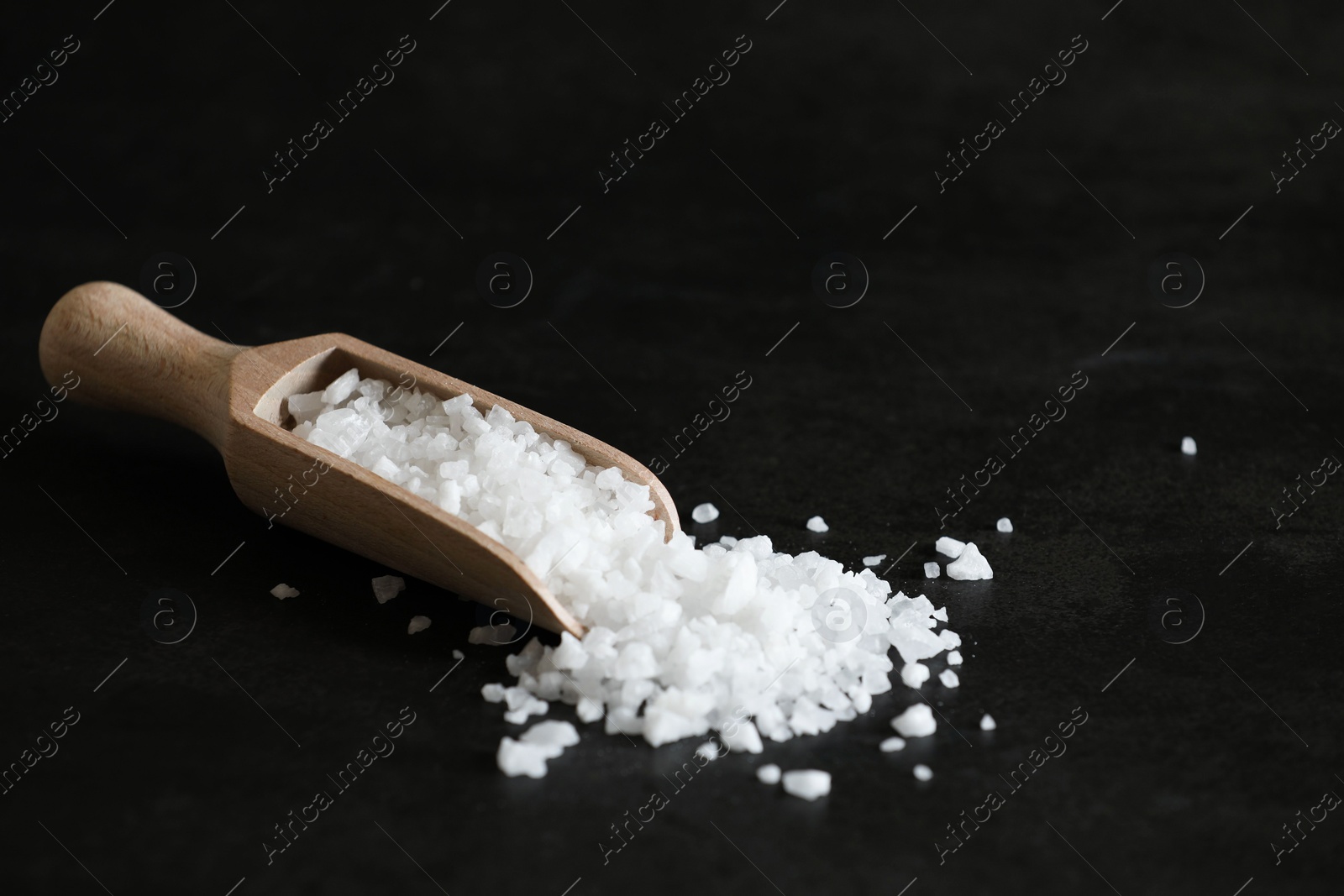 Photo of Organic salt and wooden scoop on black table. Space for text