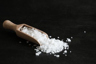 Photo of Organic salt and wooden scoop on black table. Space for text