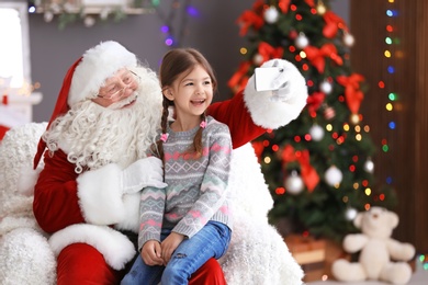 Photo of Authentic Santa Claus taking selfie with little girl indoors