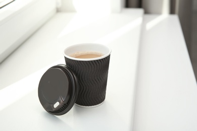 Photo of Cardboard cup of coffee on window sill indoors