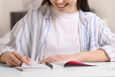 Teenage girl erasing mistake in her notebook at white desk indoors, closeup