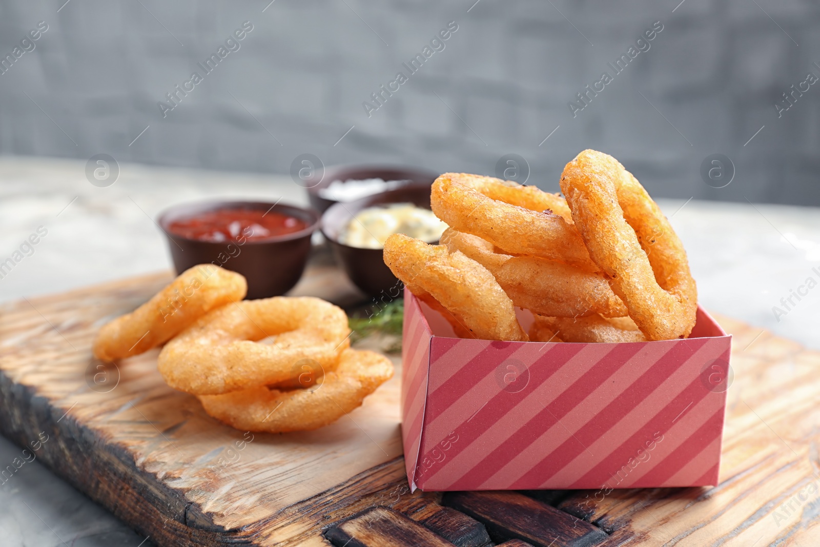 Photo of Fried onion rings served with sauces on wooden board