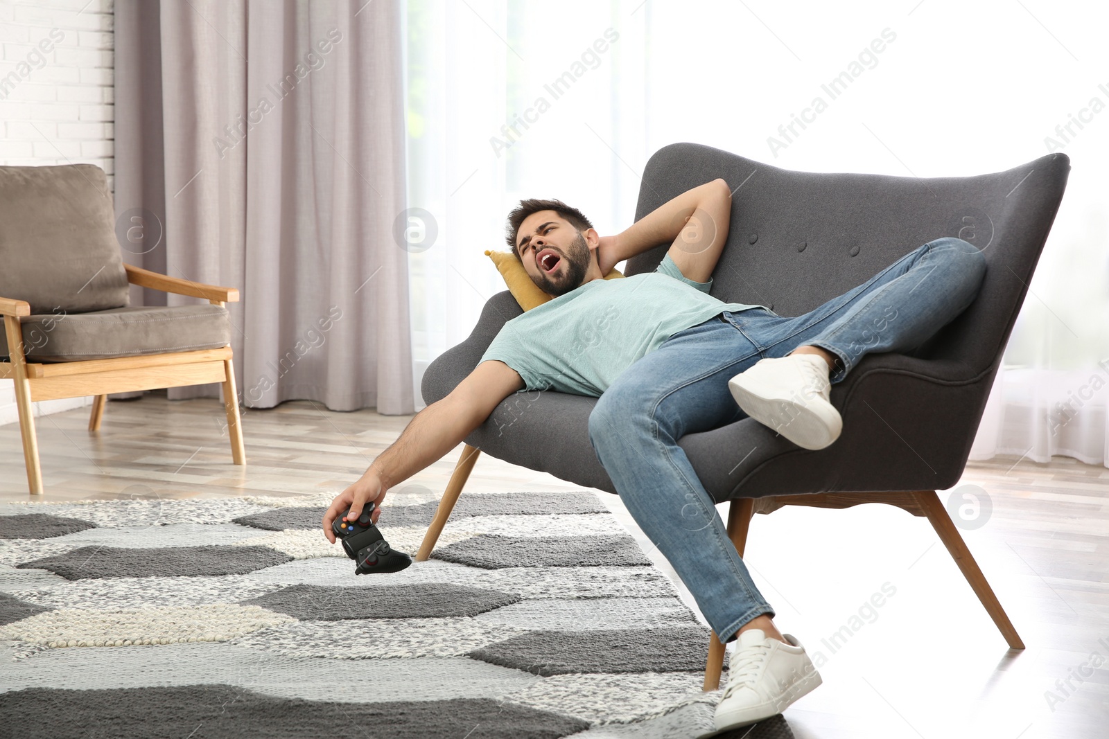 Photo of Lazy young man playing video game while lying on sofa at home