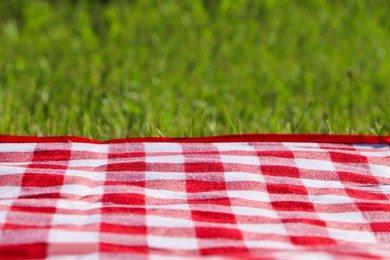 Photo of Checkered picnic tablecloth on fresh green grass, closeup