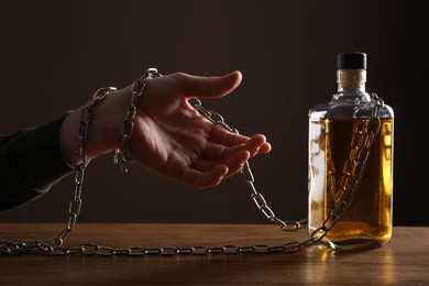 Photo of Alcohol addiction. Man chained with bottle of whiskey at wooden table, closeup