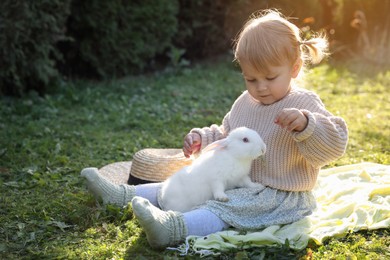 Photo of Cute little girl with adorable rabbit on green grass outdoors, space for text