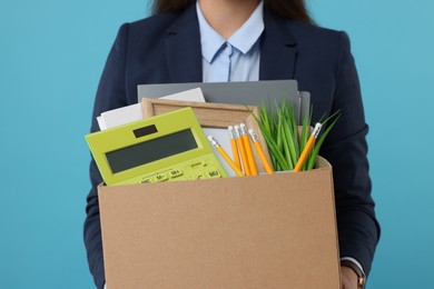 Photo of Unemployed woman holding box with personal office belongings on light blue background, closeup