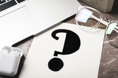Photo of Notebook with question mark, laptop and eyeglasses on grey marble table