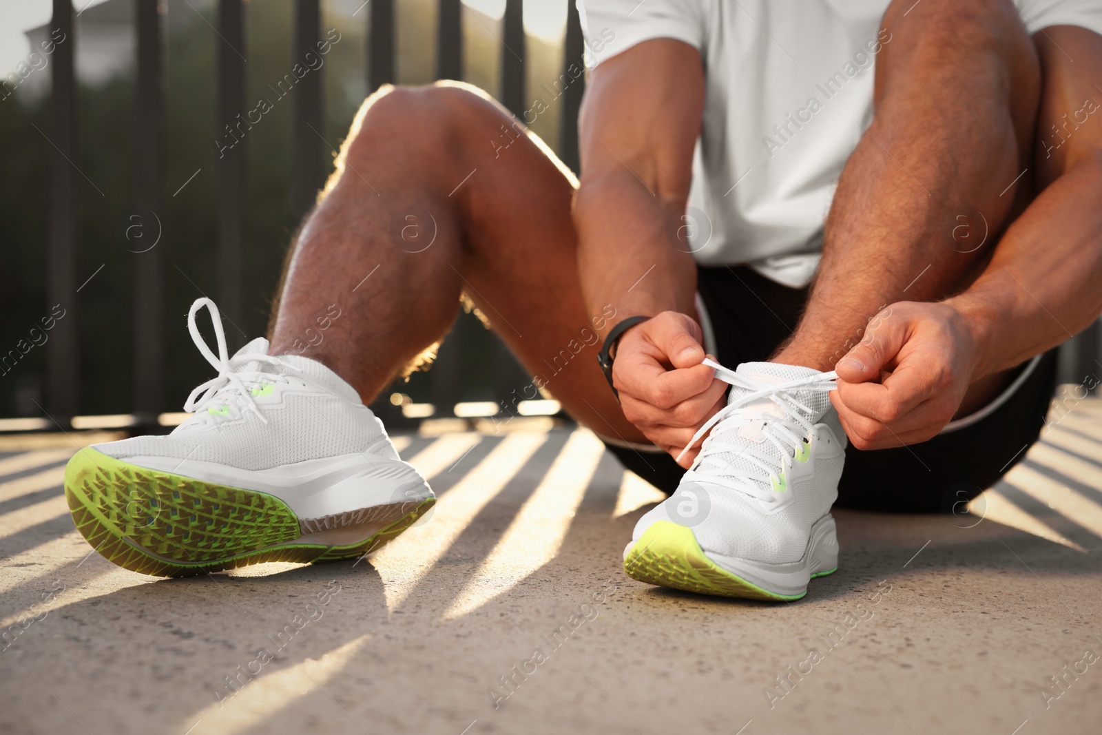 Photo of Man tying shoelaces before running outdoors on sunny day, closeup