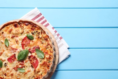 Photo of Tasty quiche with tomatoes, basil and cheese served on light blue wooden table, top view. Space for text
