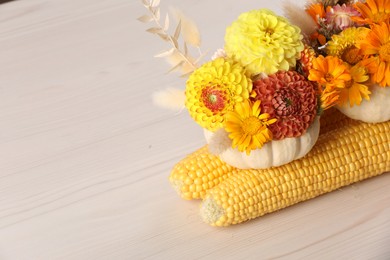 Composition of small pumpkins with beautiful flowers and corn cobs on light wooden table, closeup. Space for text