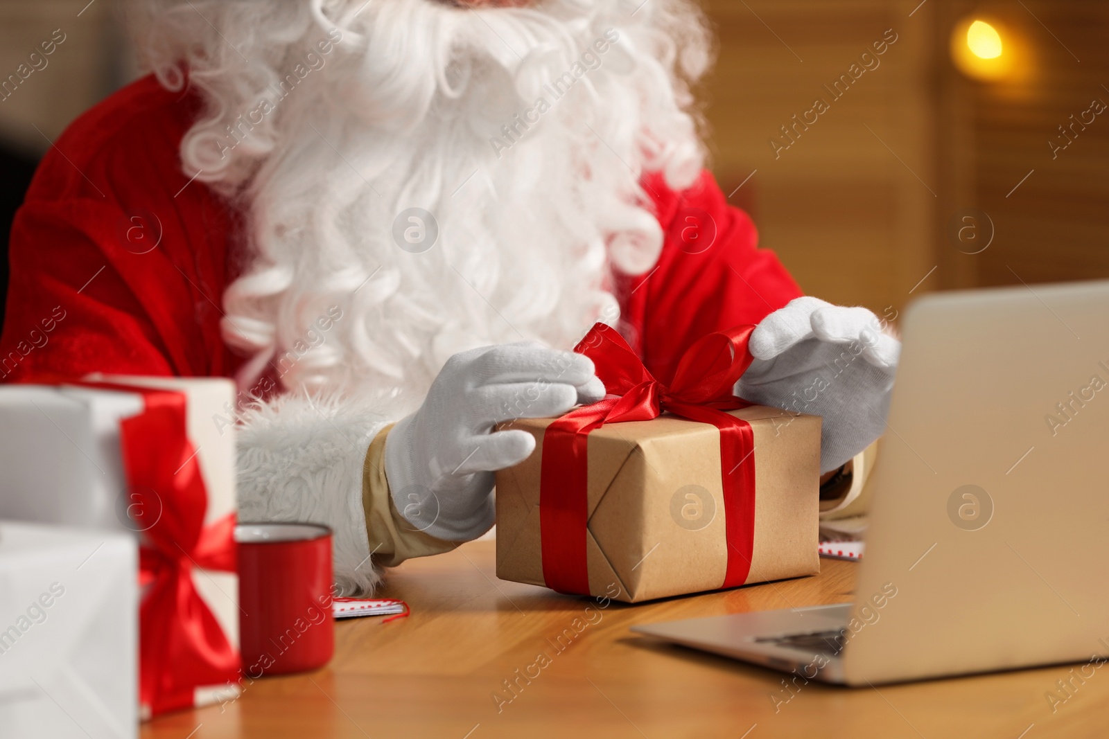 Photo of Santa Claus decorating Christmas gift with ribbon at home, closeup