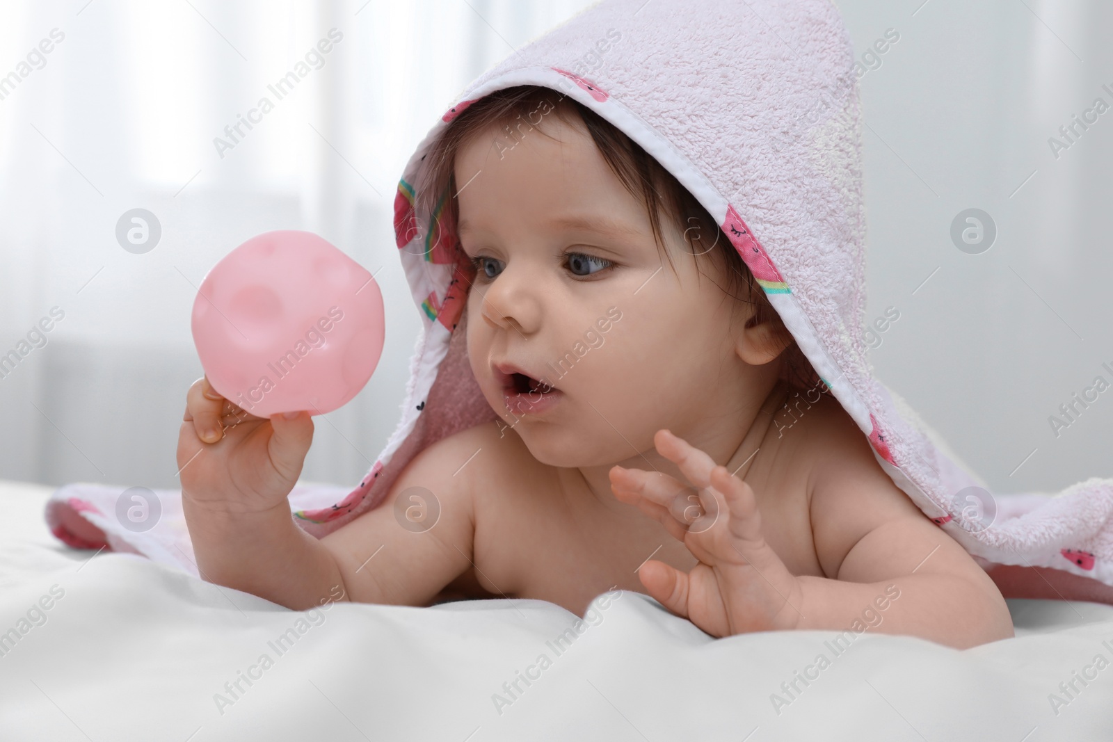 Photo of Cute little baby with toy in hooded towel after bathing on bed at home