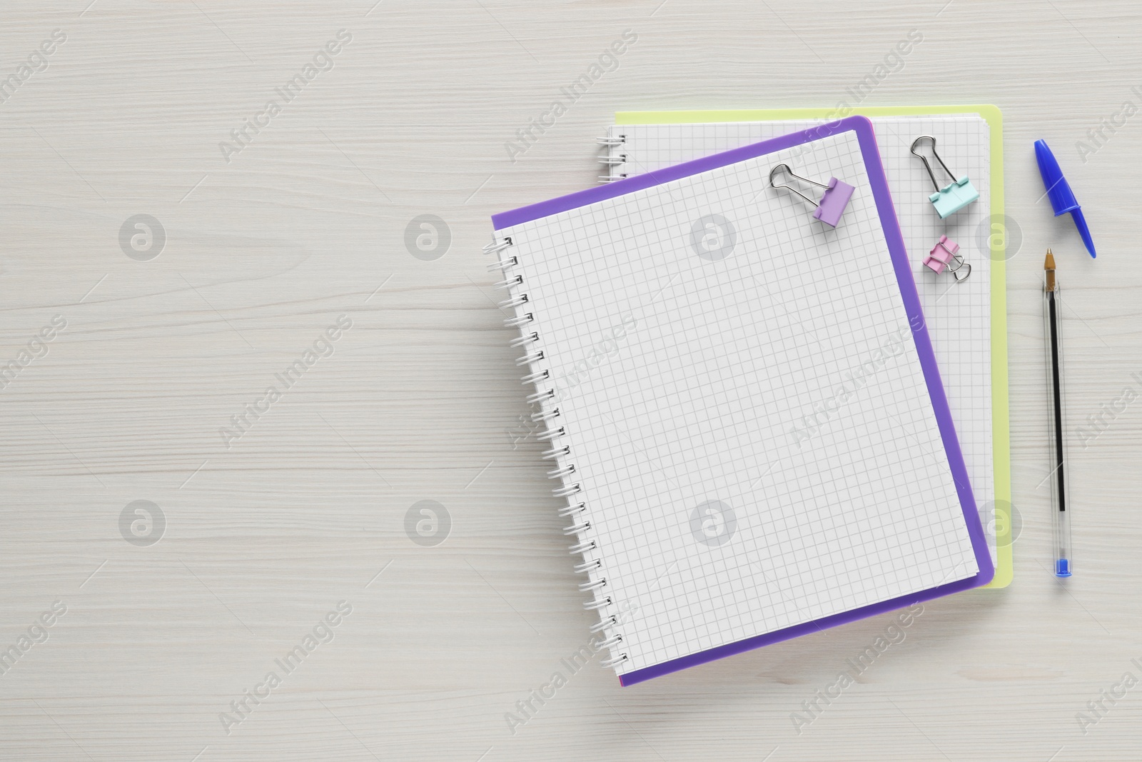 Photo of Ballpoint pen, notebooks and binder clips on wooden table, flat lay. Space for text