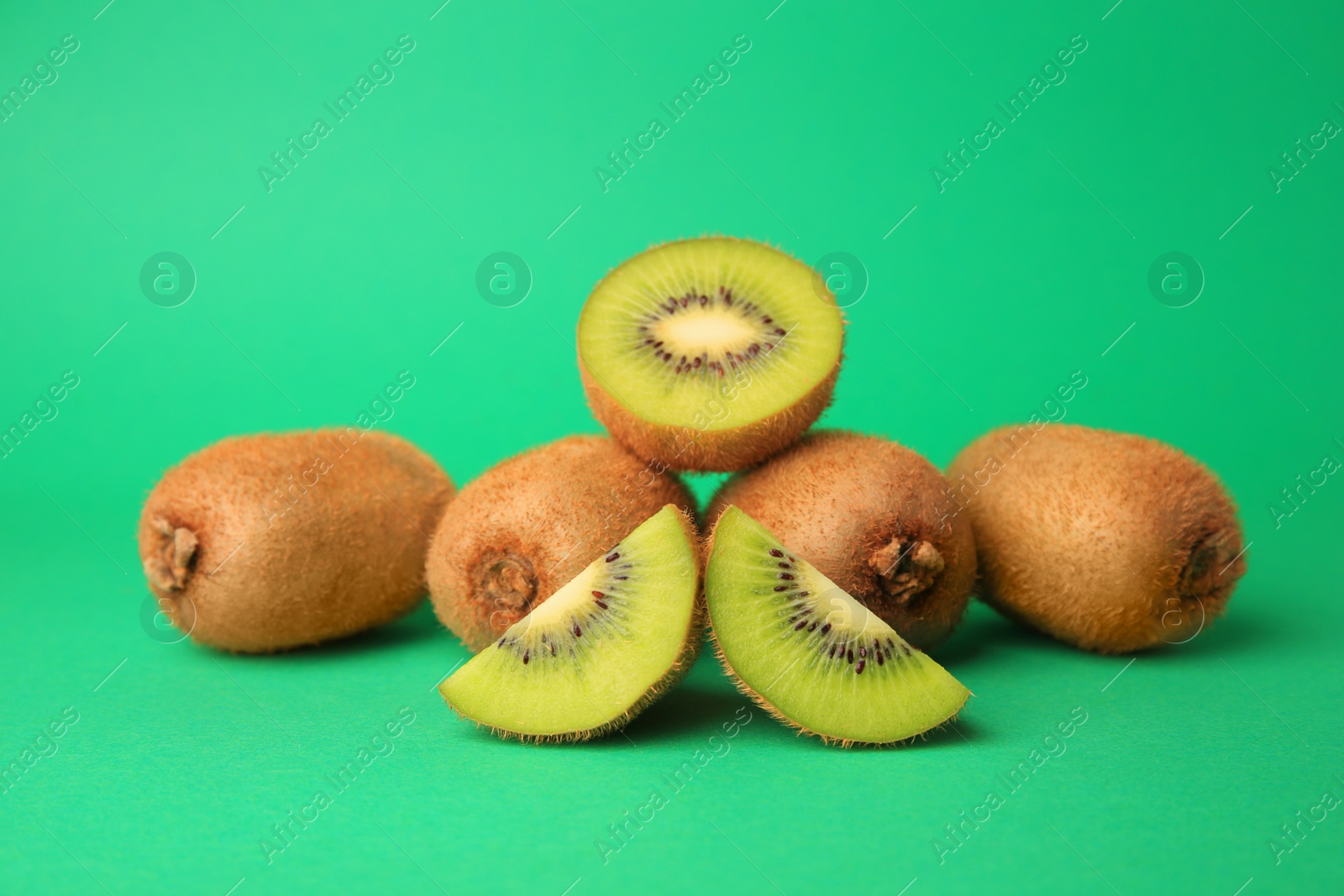 Photo of Heap of whole and cut fresh kiwis on green background