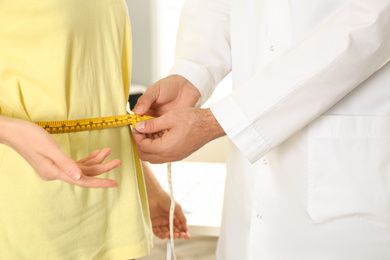Nutritionist measuring patient's waist in clinic, closeup