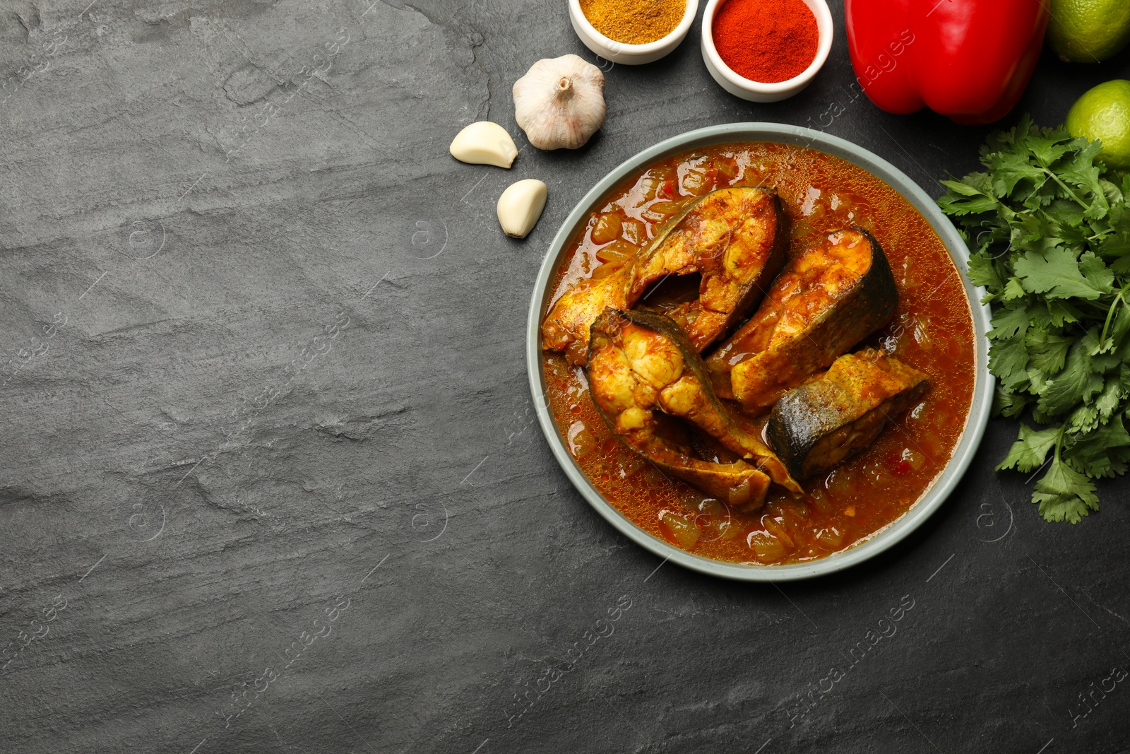 Photo of Tasty fish curry and ingredients on grey table, flat lay. Space for text. Indian cuisine