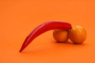 Photo of Chili pepper and tangerines symbolizing male sexual organ on orange background. Potency problem