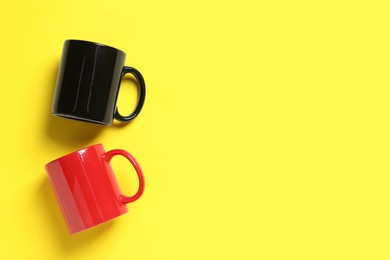 Photo of Black and red ceramic mugs on yellow background, flat lay. Space for text