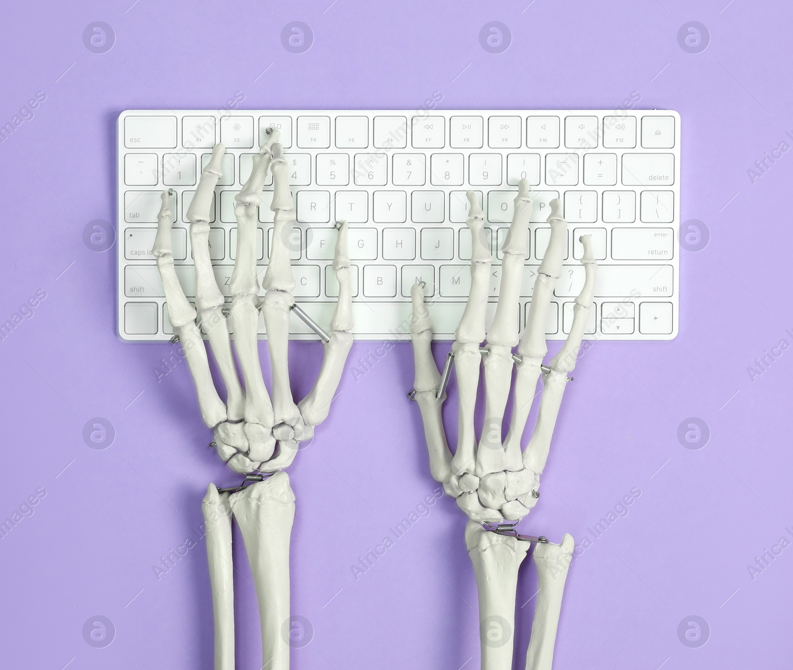 Photo of Human skeleton using computer keyboard on violet background, top view