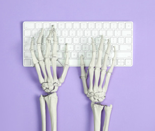 Human skeleton using computer keyboard on violet background, top view