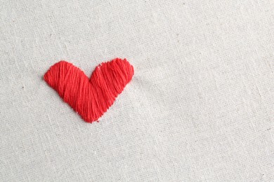 Photo of Embroidered red heart on light cloth, top view. Space for text