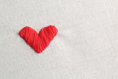 Embroidered red heart on light cloth, top view. Space for text