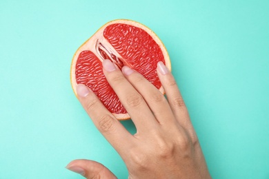 Photo of Young woman touching half of grapefruit on turquoise background, top view. Sex concept
