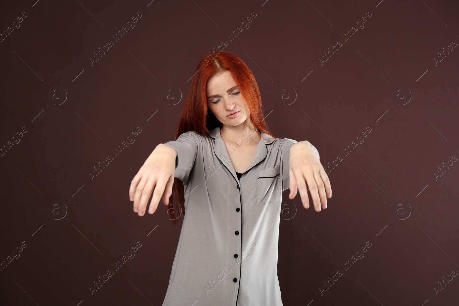 Photo of Young woman wearing pajamas in sleepwalking state on brown background