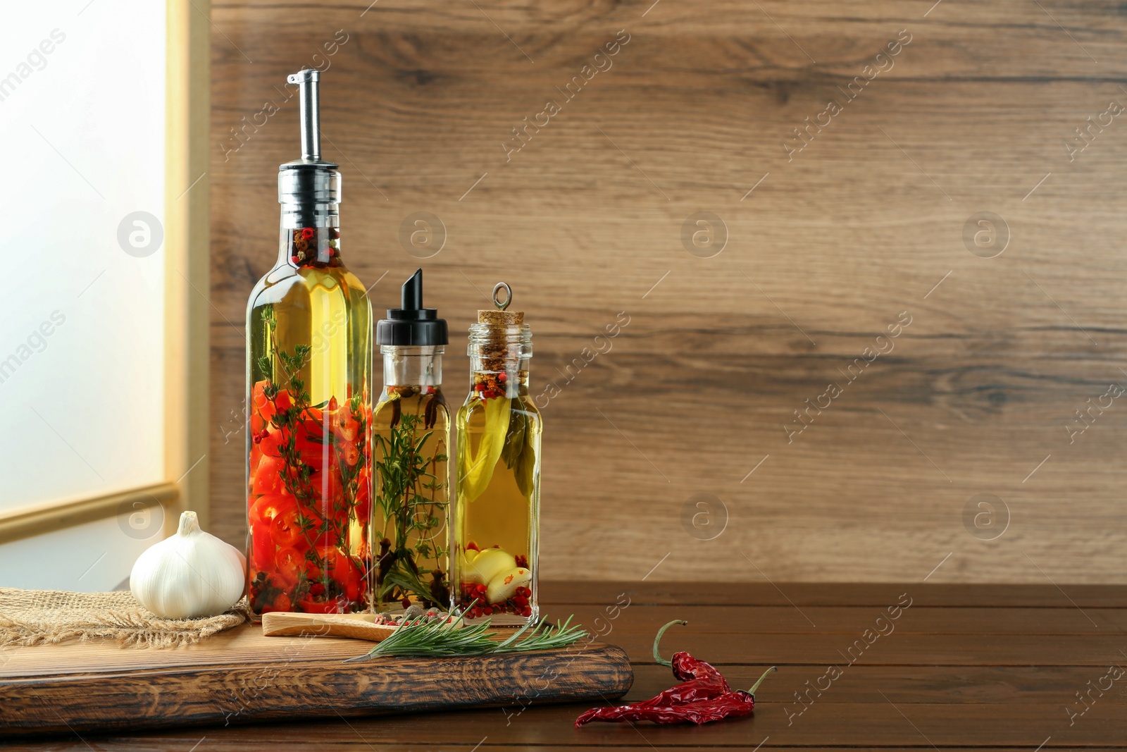 Photo of Cooking oil with different spices and herbs in bottles on wooden table. Space for text