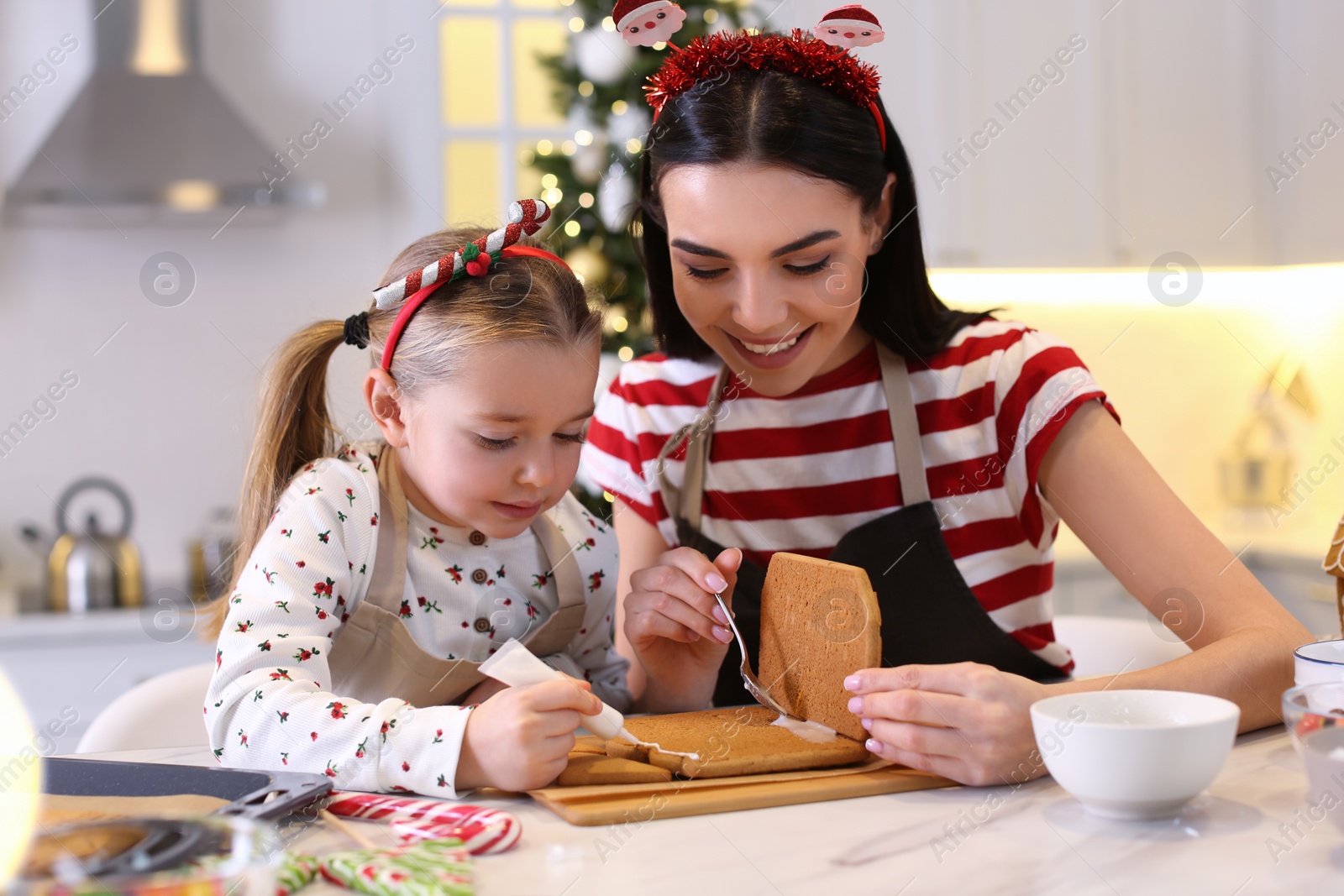 Photo of Mother and daughter making gingerbread house at table indoors