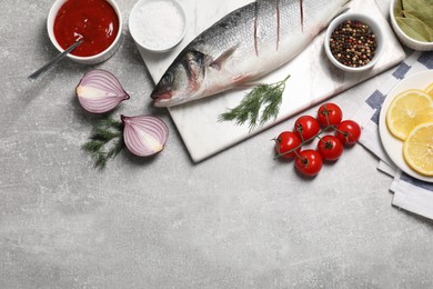 Photo of Fresh raw sea bass fish and ingredients on light gray table, flat lay. Space for text