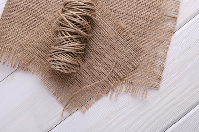 Spool of thread and burlap fabric on white wooden table, top view