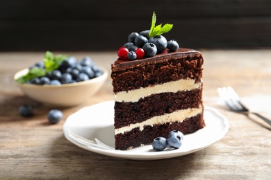 Photo of Plate with slice of chocolate sponge berry cake on wooden table