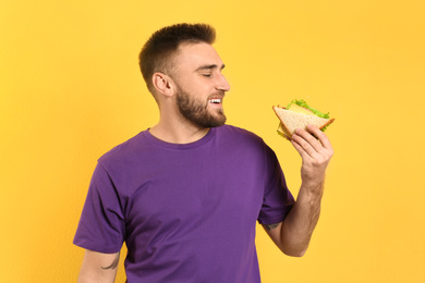 Young man eating tasty sandwich on yellow background