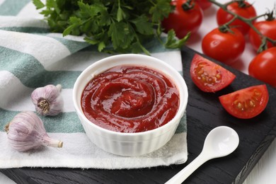 Photo of Organic ketchup in bowl, fresh tomatoes and garlic on table. Tomato sauce