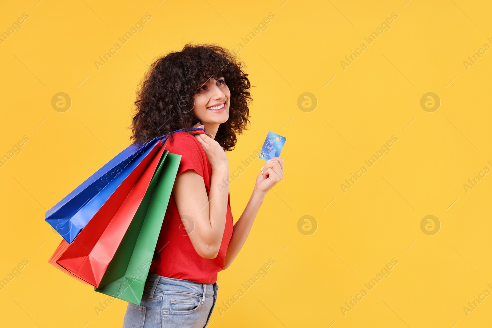 Photo of Happy young woman with shopping bags and credit card on yellow background. Space for text
