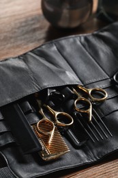 Photo of Hairdresser tools. Professional scissors and combs in leather organizer on wooden table, closeup