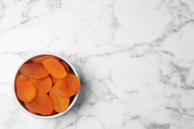 Photo of Bowl of apricots on marble background, top view with space for text. Dried fruit as healthy food